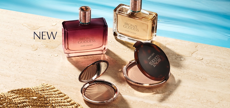 The Bronze Goddess Fragrance Collection with two bottles in the background and bronzer palettes in the foreground. The image has a background of the products sitting on the beach with the ocean in the background.